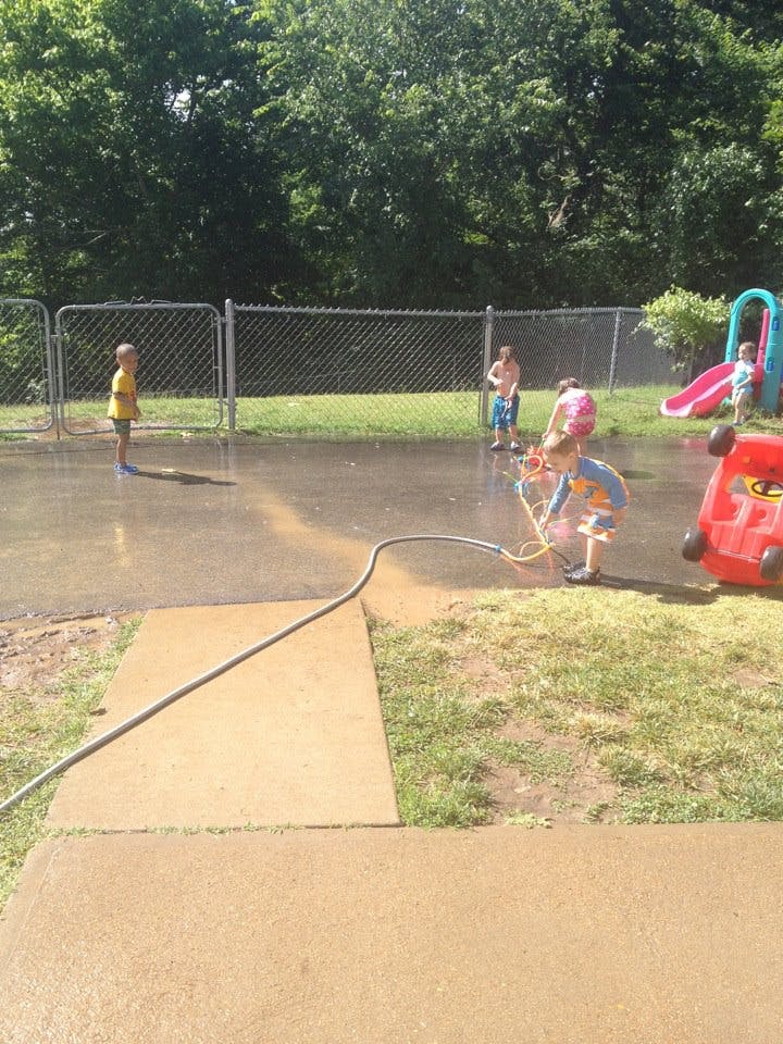 Children playing in water on a paved area with a hose