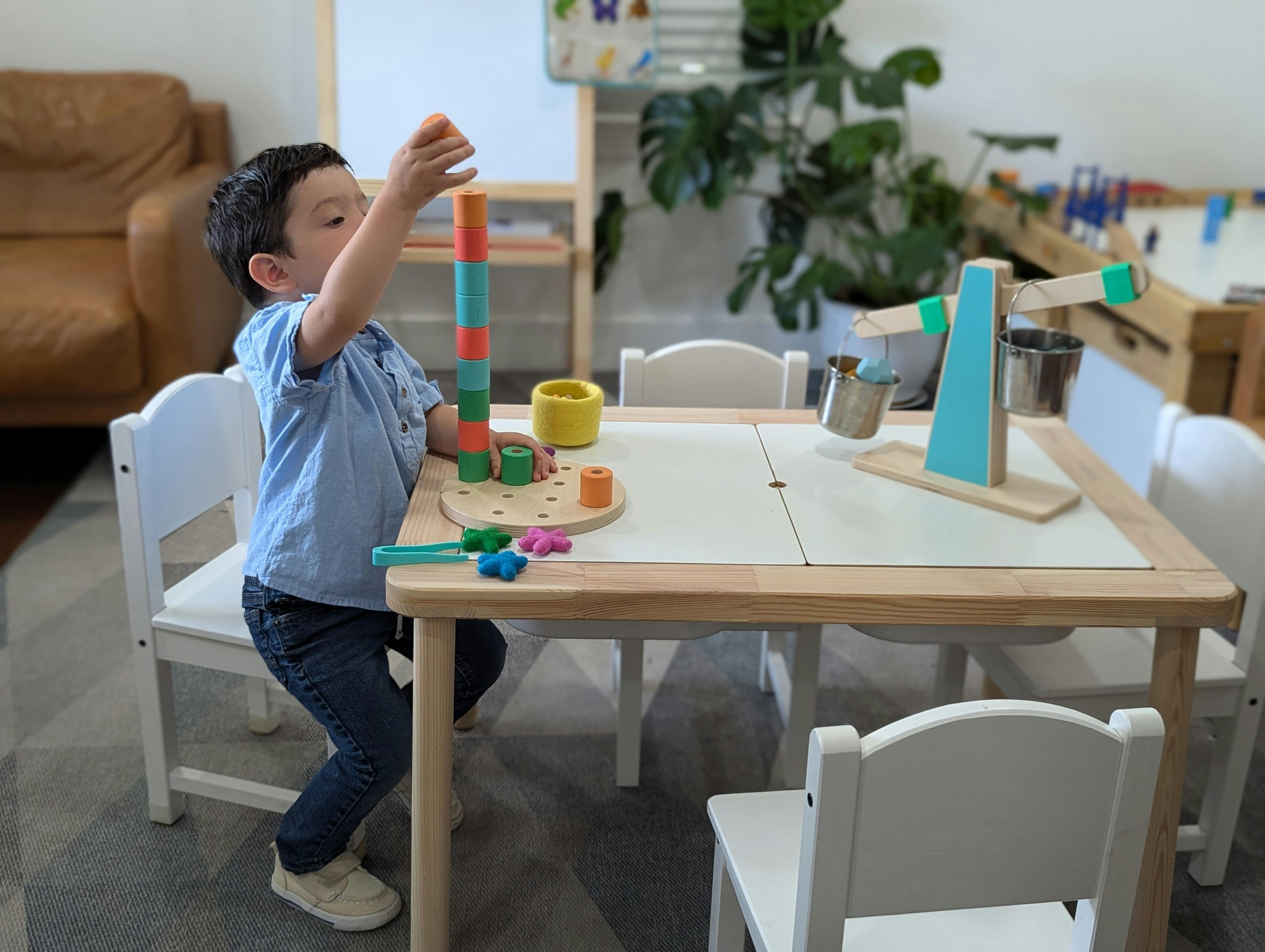 Child standing at a table, stacking colorful blocks