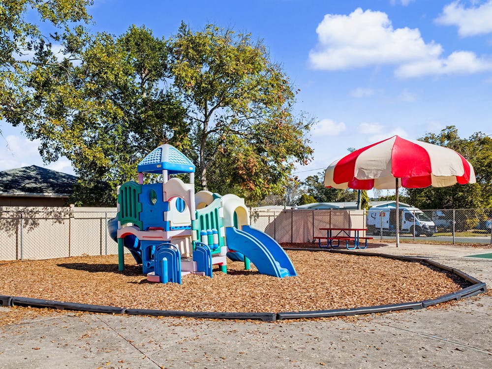 Colorful playground structure with slides on wood chips next to a red and white umbrella
