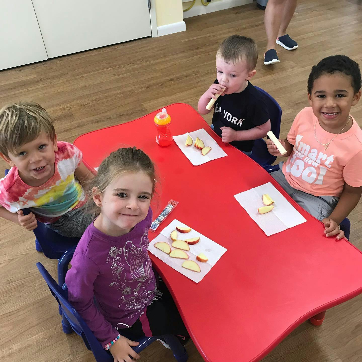 Four children sitting at a red table with apple slices