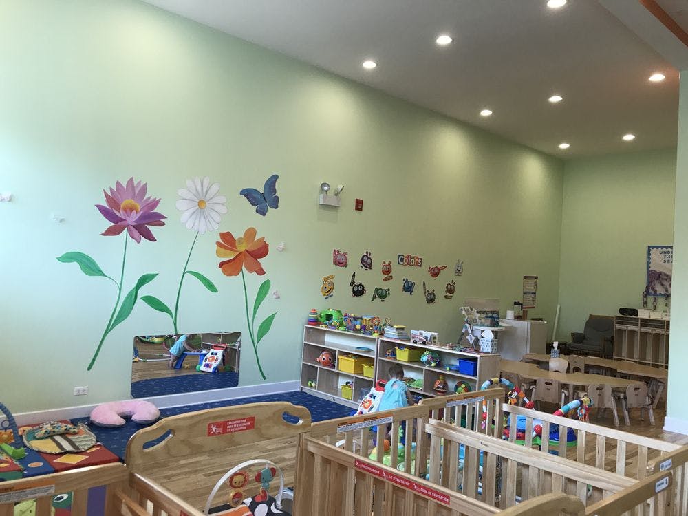 Nursery room with cribs, shelves of toys, and flower wall decals