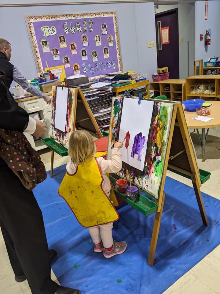 Child in a yellow smock painting at an easel