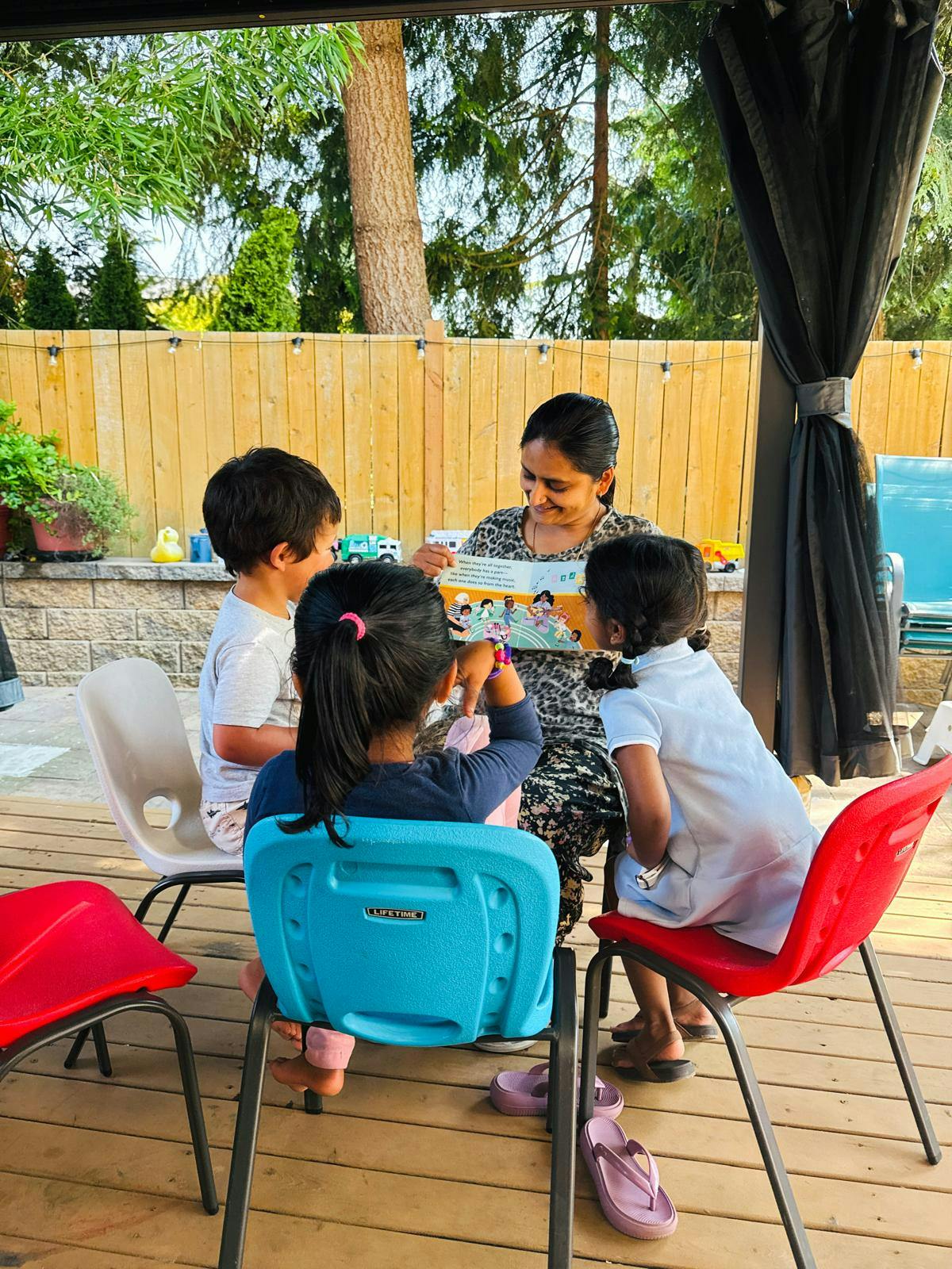 Adult reading a book to three children on a backyard deck
