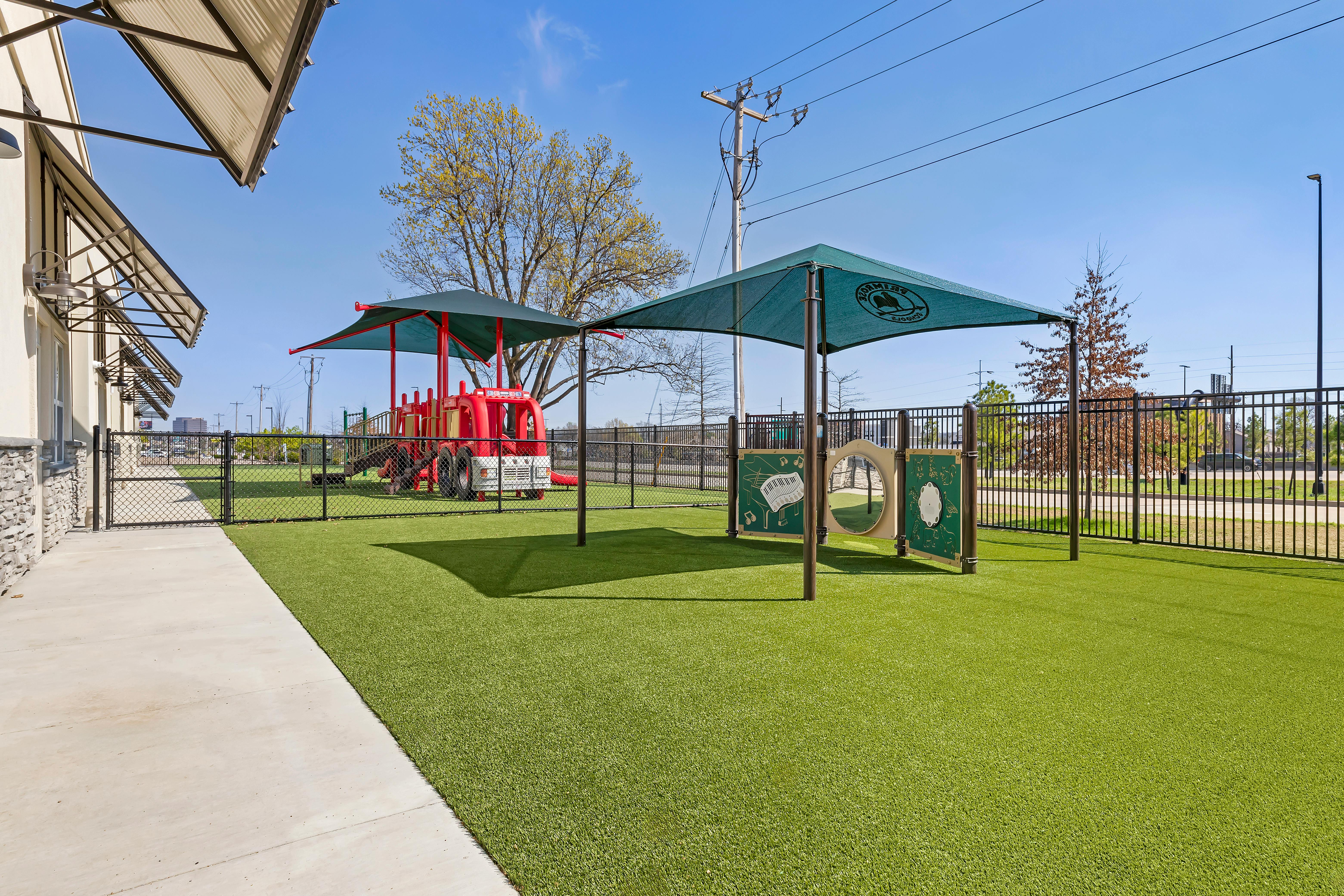 Playground with green turf, shaded play structures, and a red fire truck