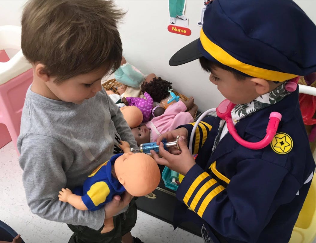 Child in uniform giving a shot to a baby doll held by another child