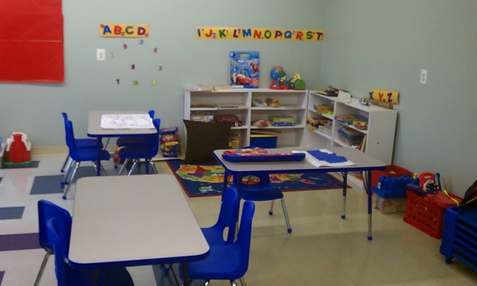 Classroom with small tables and chairs, shelves with toys, and alphabet letters on wall