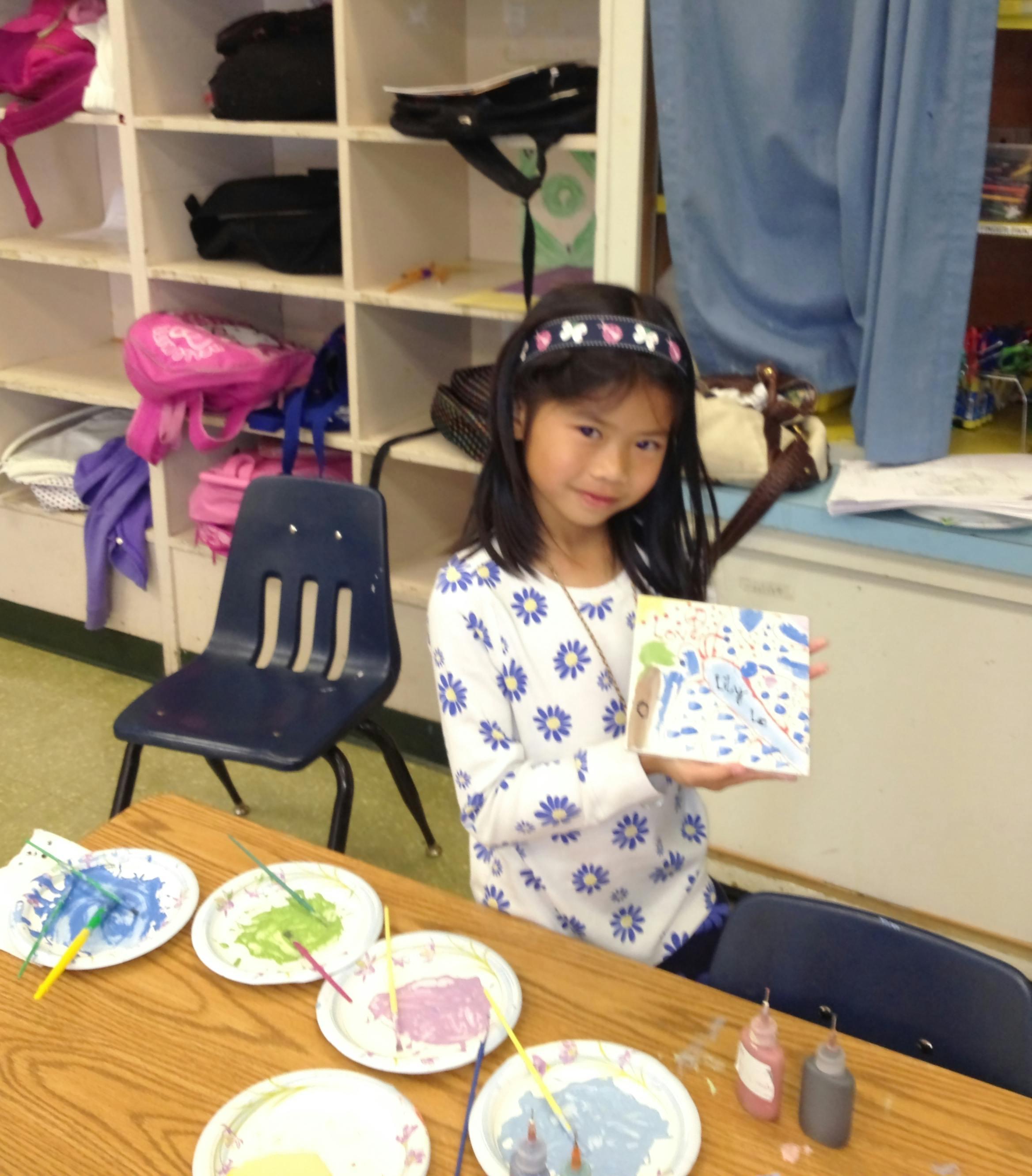 Child holding up a small painting in a classroom