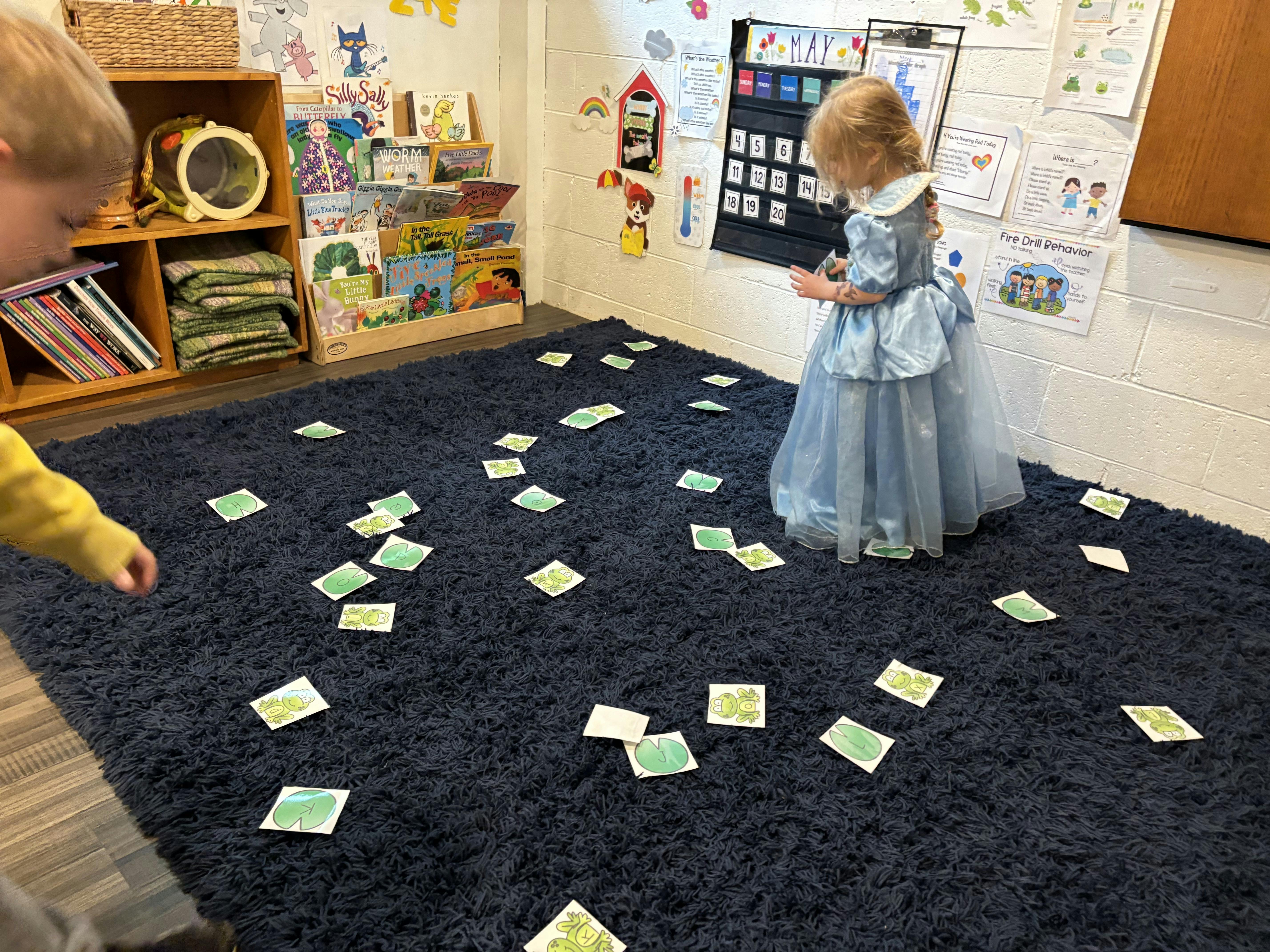 Two children playing with cards on a dark blue rug in a classroom