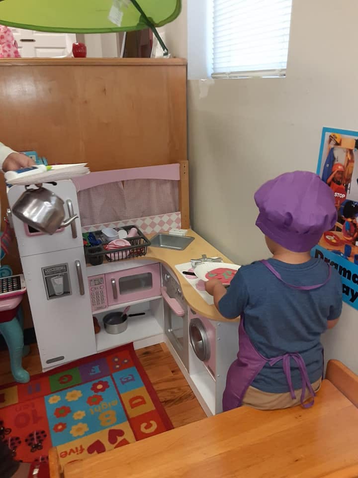 Child in a purple chef's hat and apron playing with a toy kitchen set