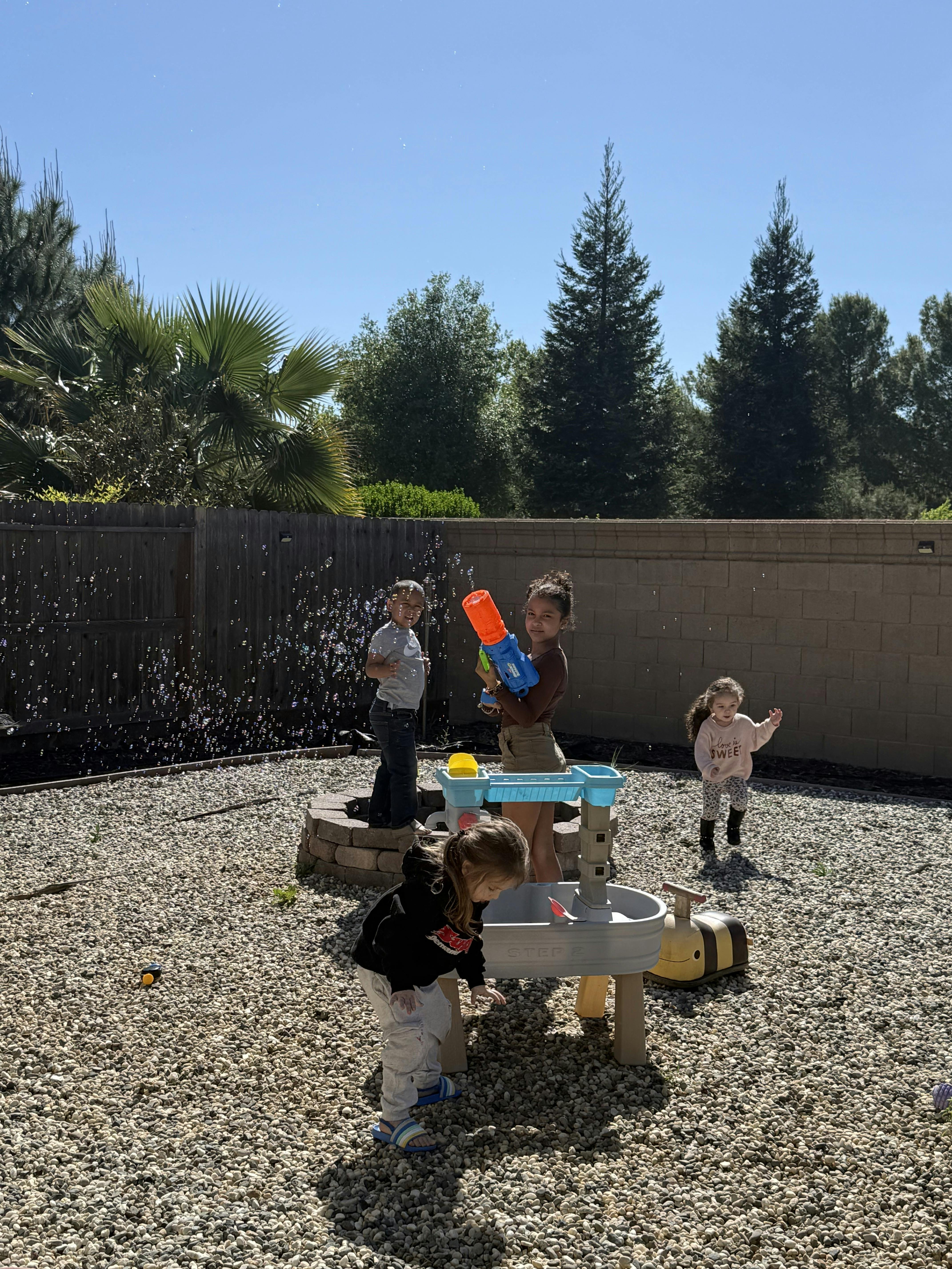 Four children playing with bubbles and a water table in a backyard