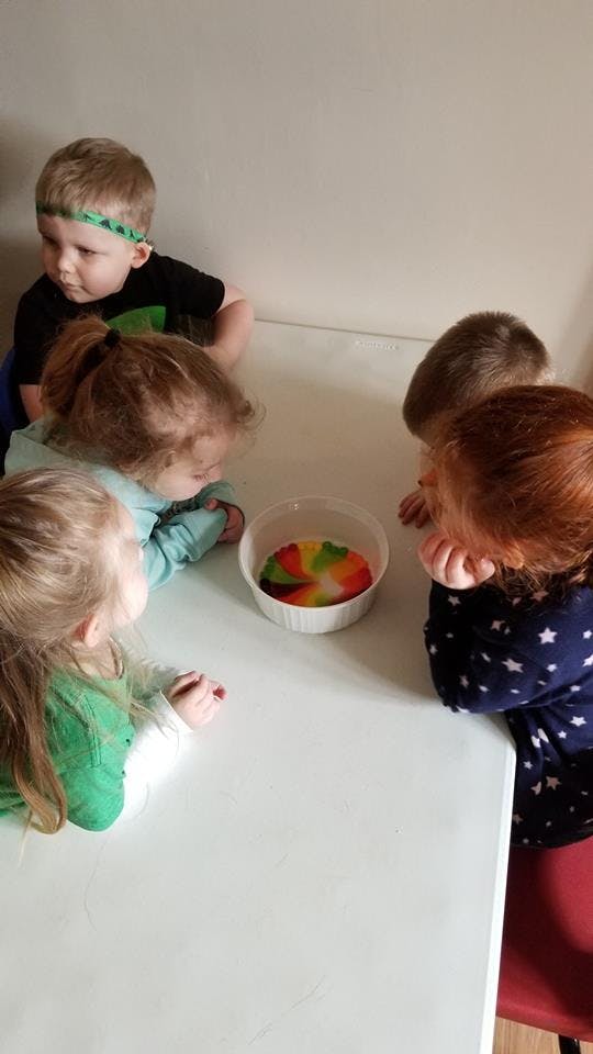 Children gathered around a table looking at a bowl with colorful liquid