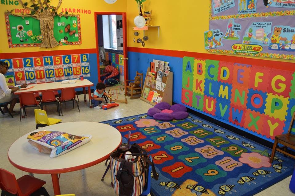 Classroom with alphabet and number decorations, people at tables, and a child on the floor