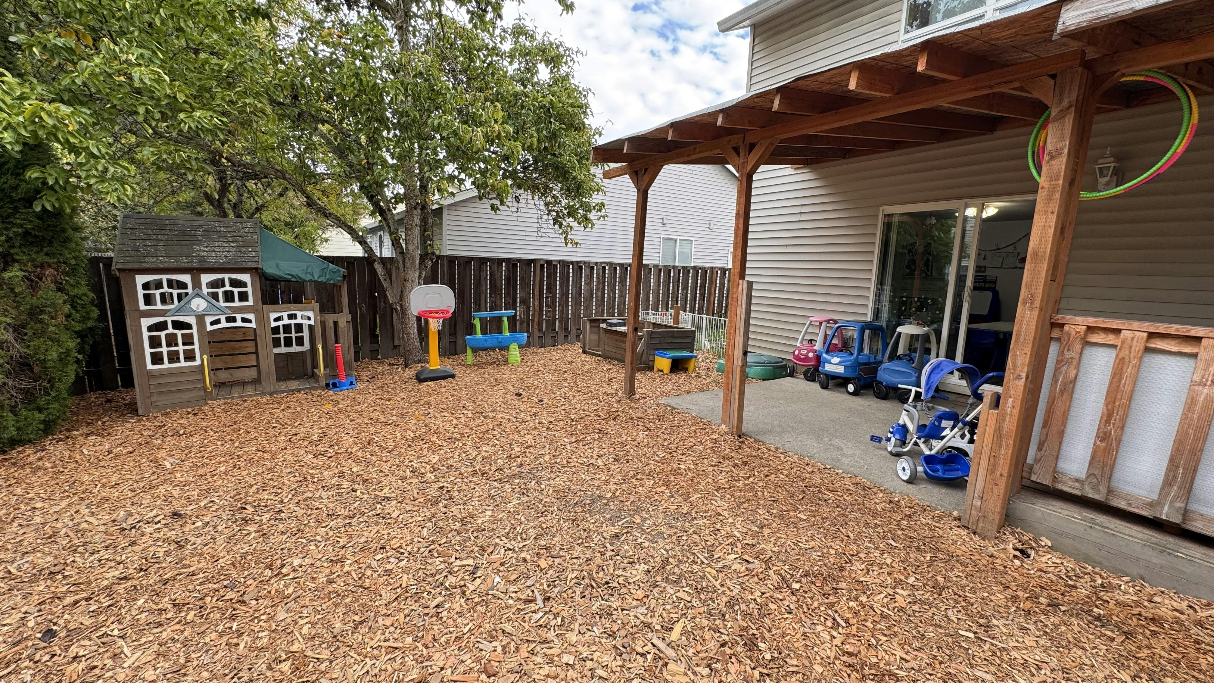 Backyard with wood chips, playhouse, and covered patio