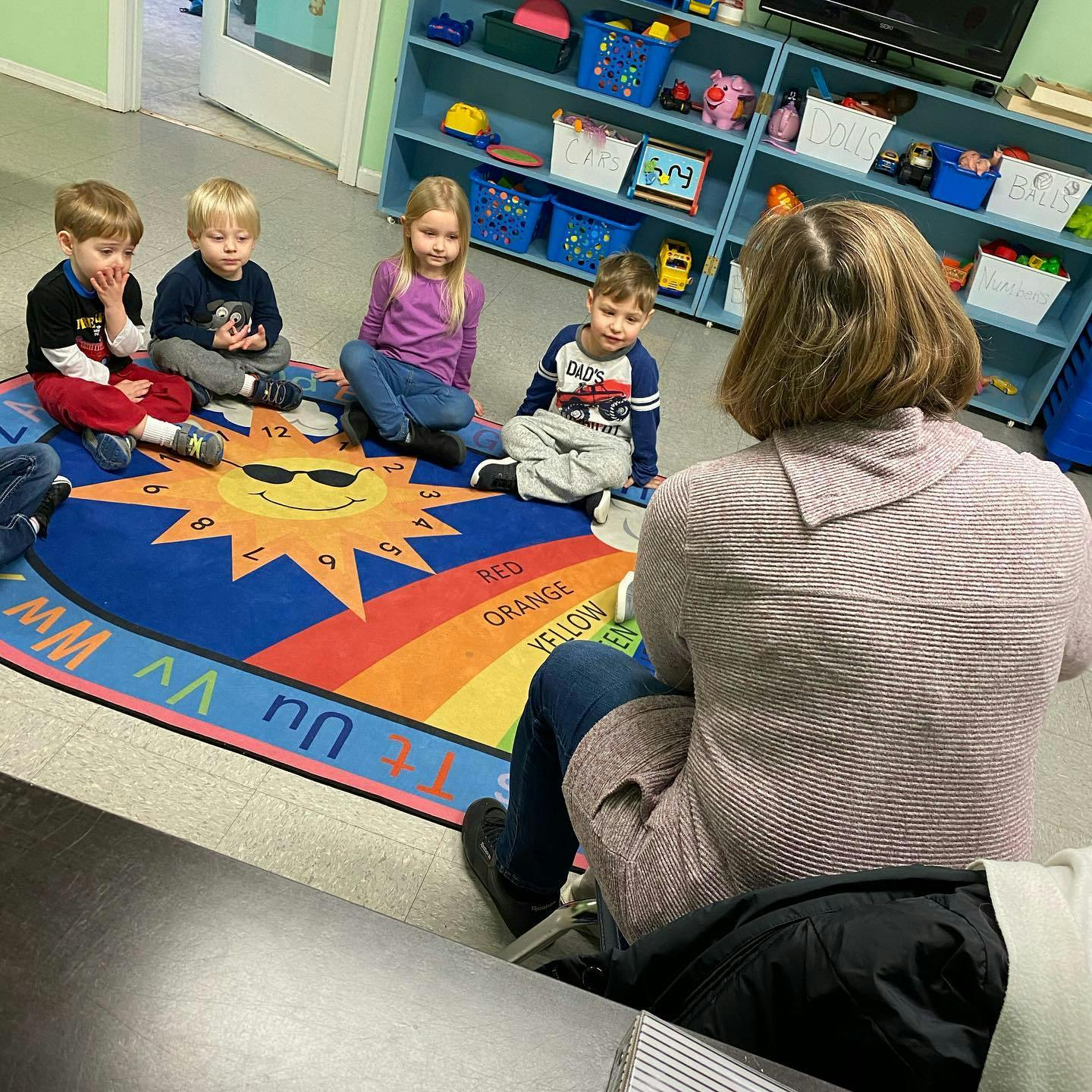 Adult and four children sitting on a rug in a classroom