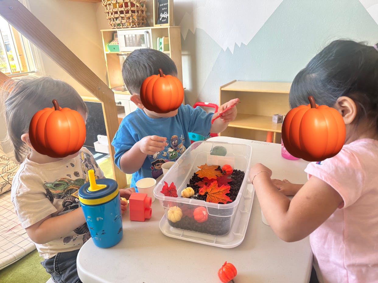 Three children playing with a sensory bin at a table