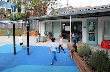 Children playing on a blue playground surface outside a building