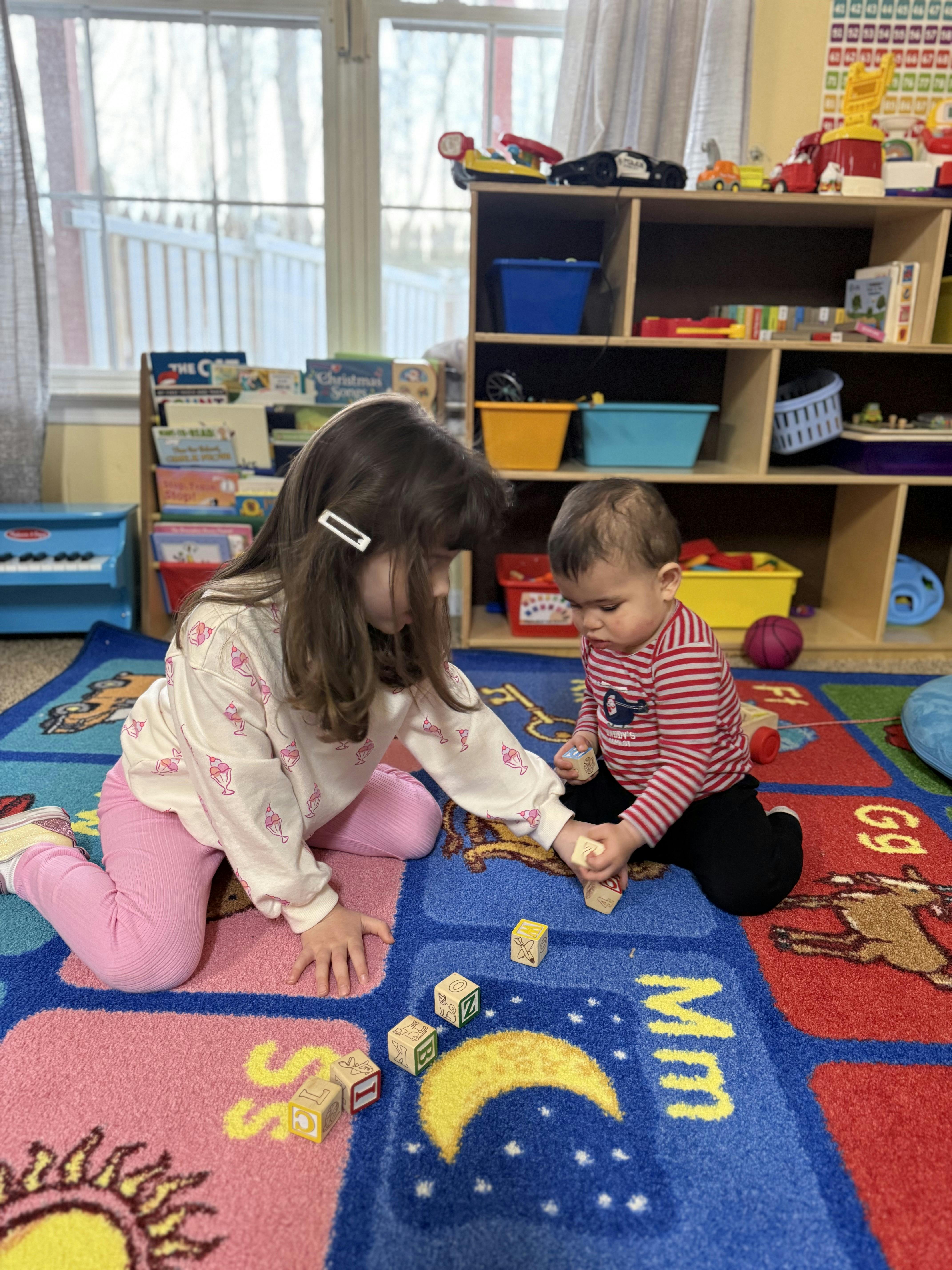 Two children playing with alphabet blocks on a colorful rug