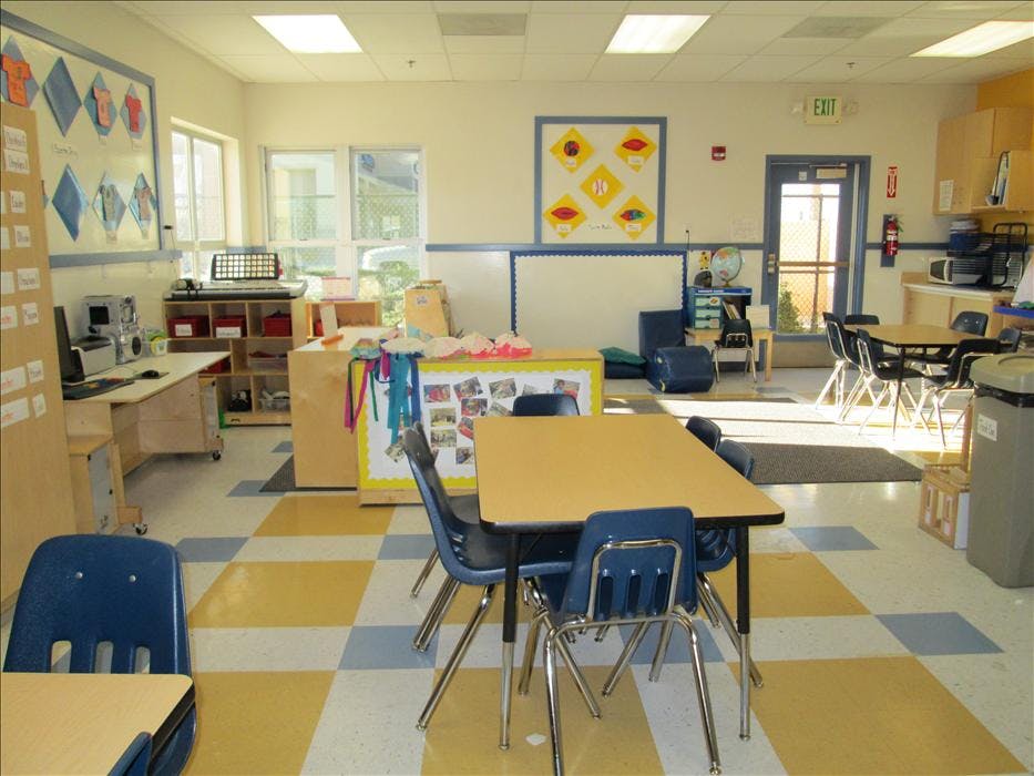 Empty classroom with small tables and chairs, bright windows