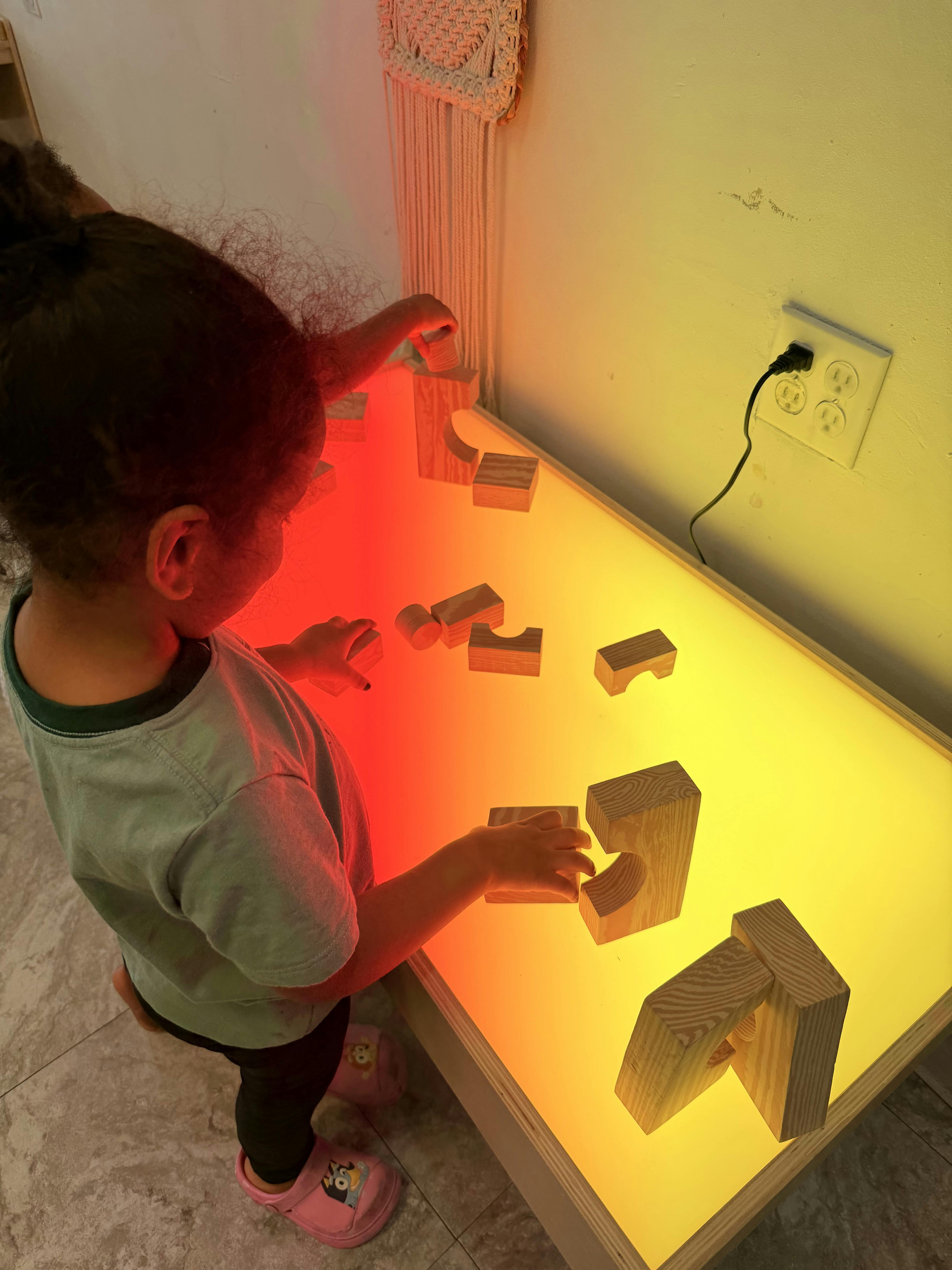 Child playing with wooden blocks on a light-up table