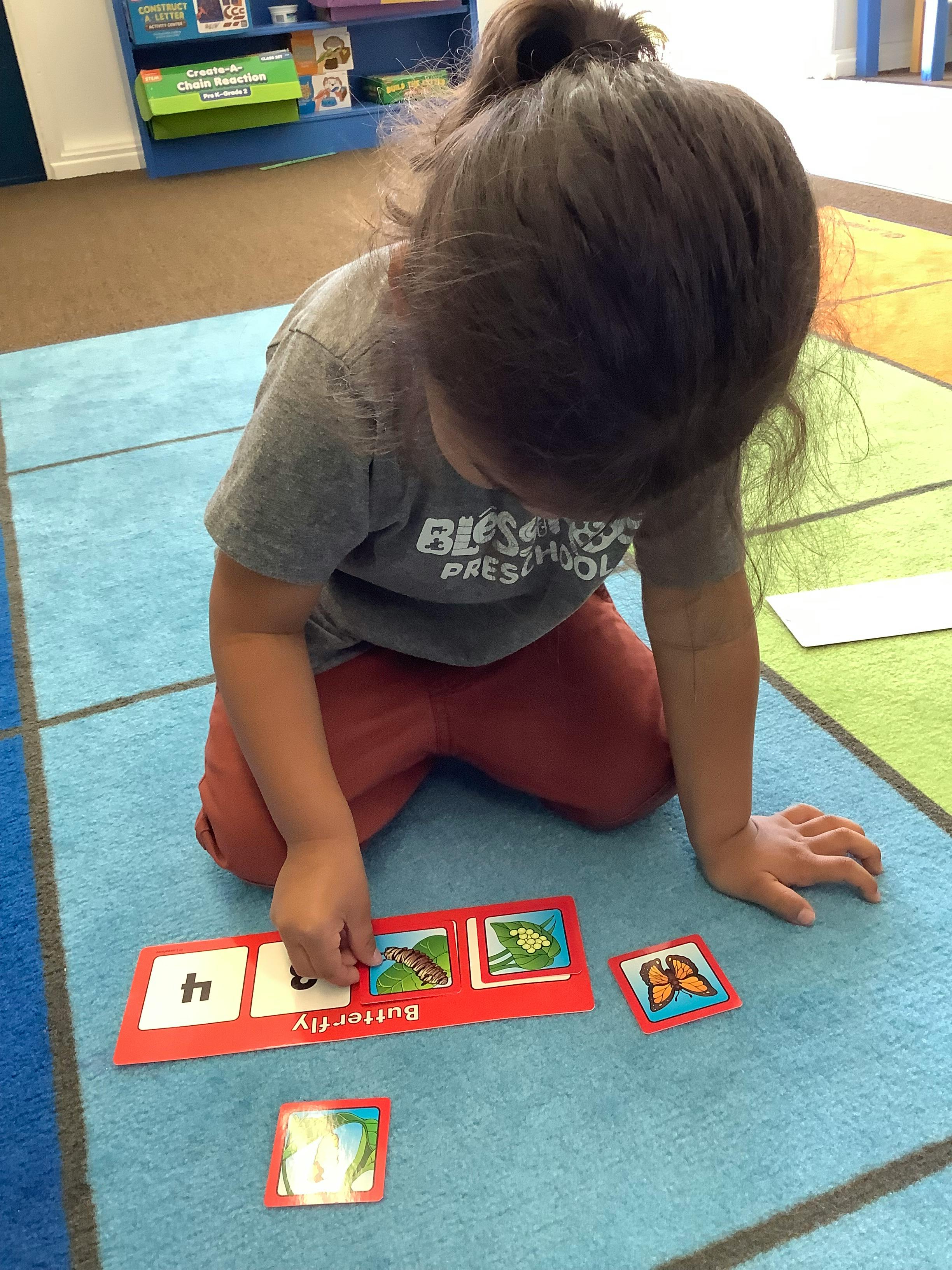 Child kneeling on a rug, placing a card on a learning mat