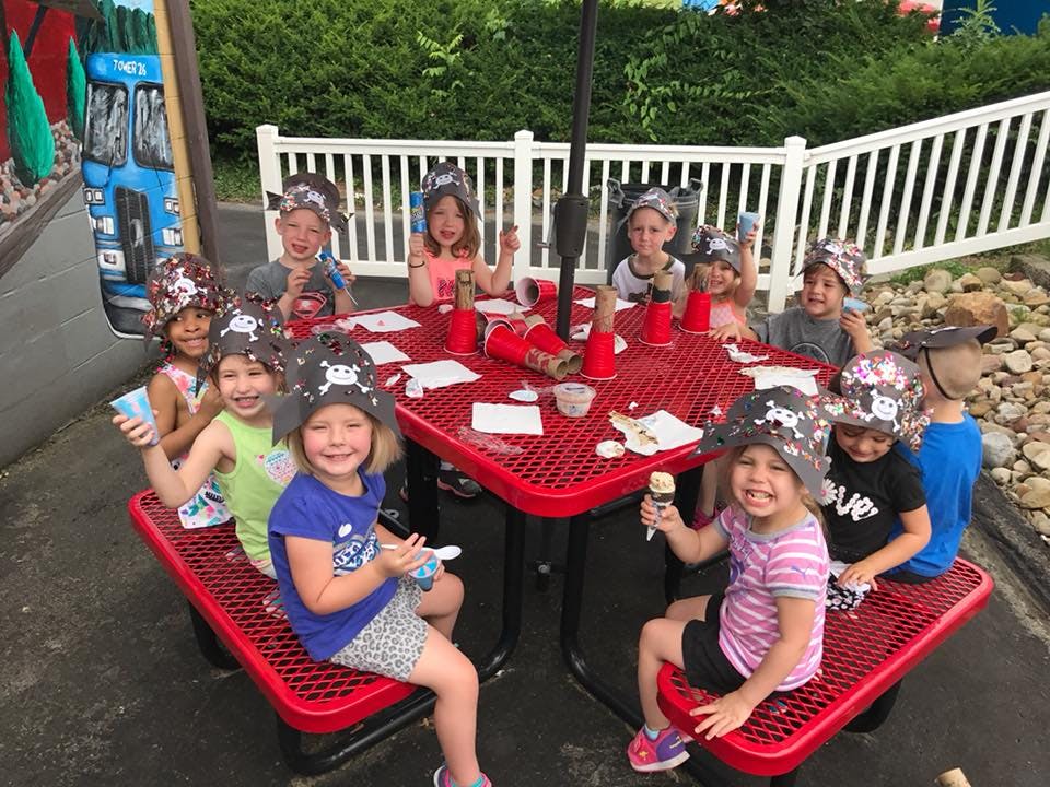 Children wearing pirate hats sitting around a red picnic table