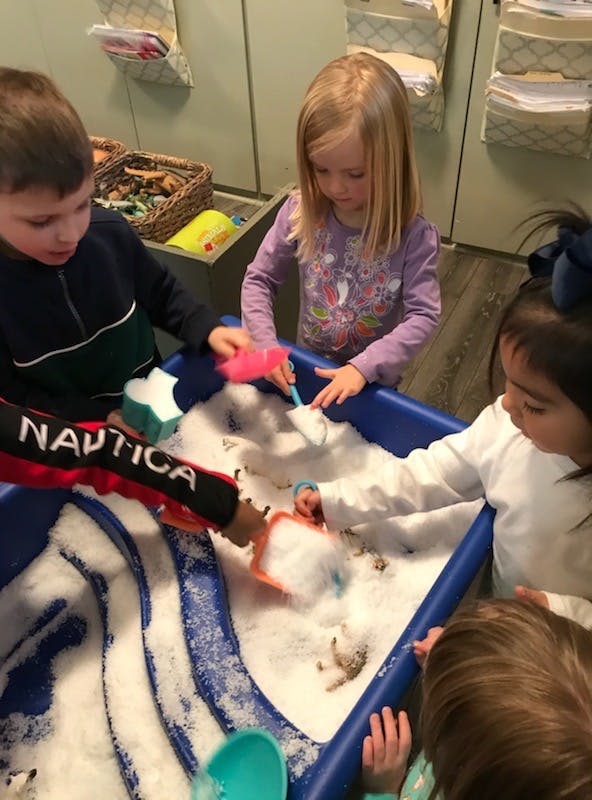 Children playing with snow in a blue bin