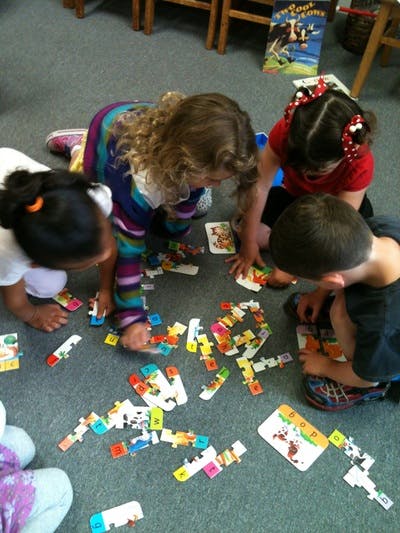 Four children on the floor playing with puzzle pieces