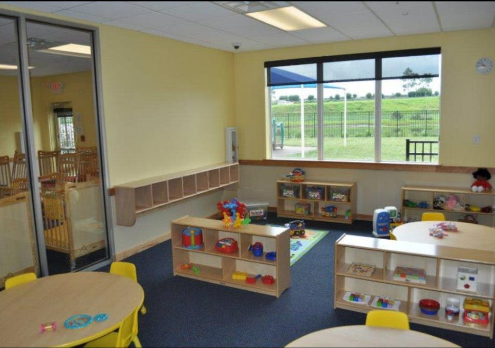 Empty classroom with small tables, shelves of toys, and large window