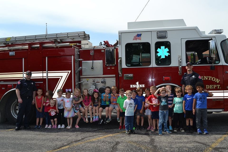 Two people in uniform with a group of children in front of a fire truck
