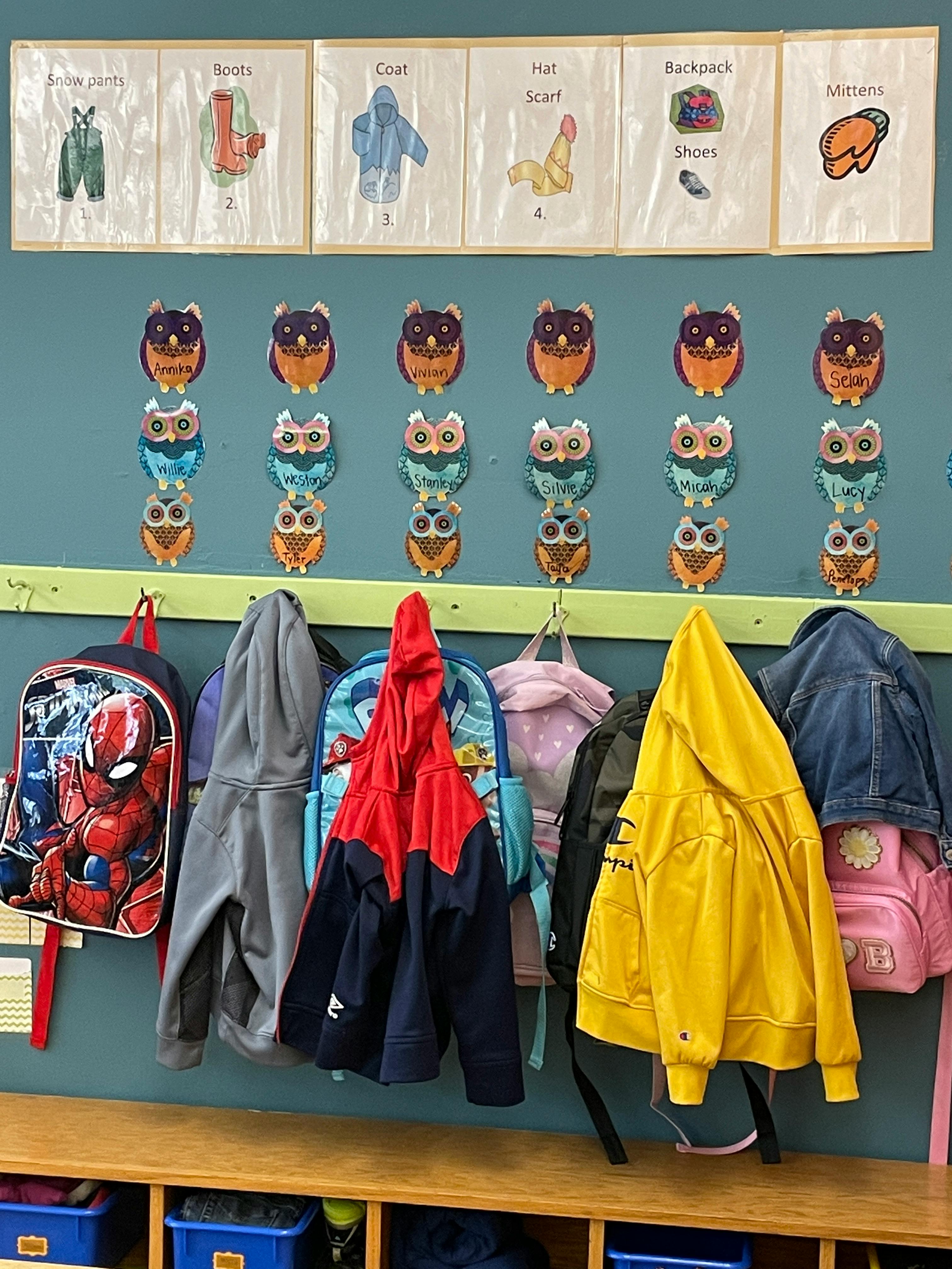 Backpacks and jackets hanging on hooks below owl decorations and clothing charts