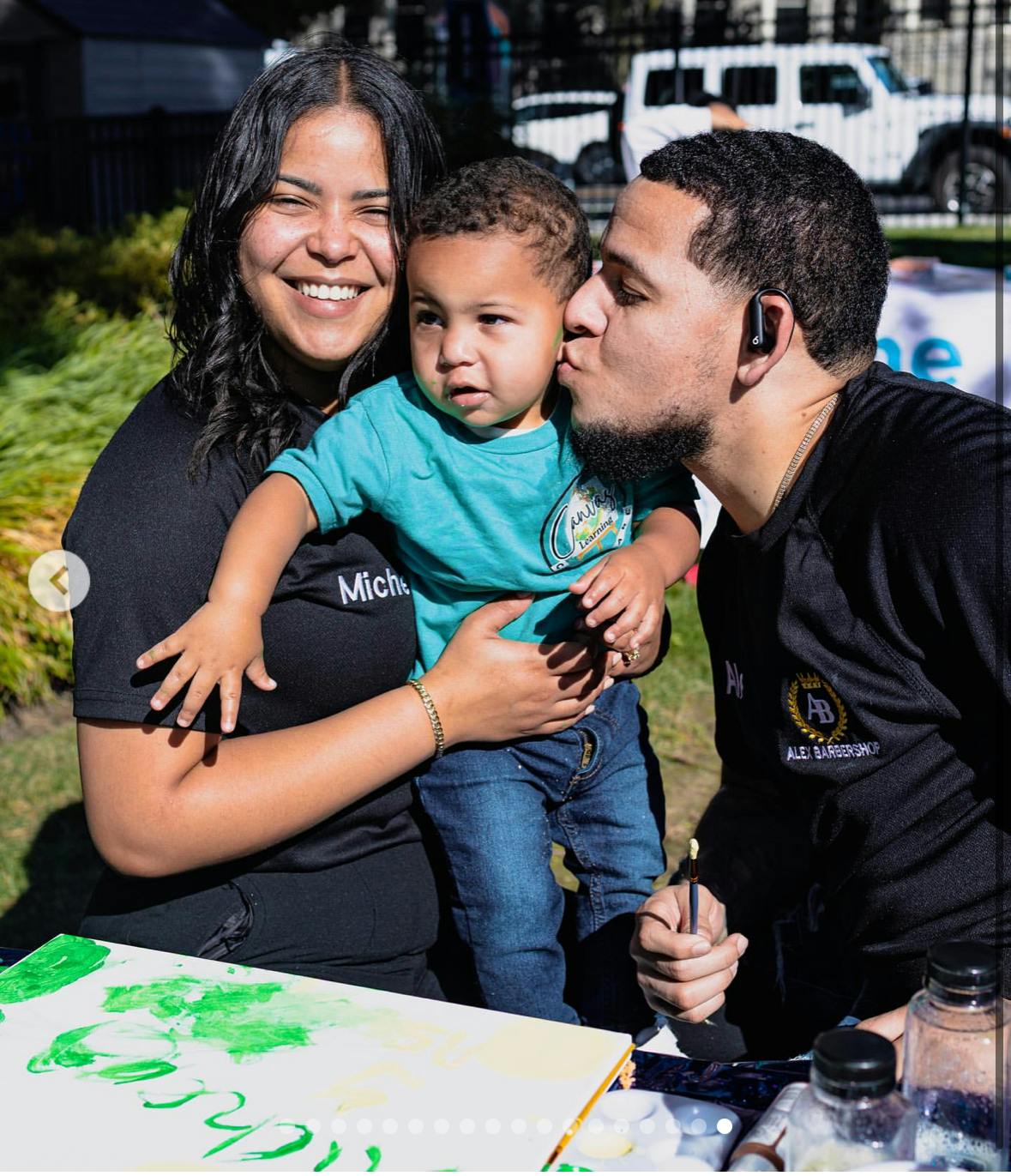 Adult kissing the cheek of a child held by another adult while painting