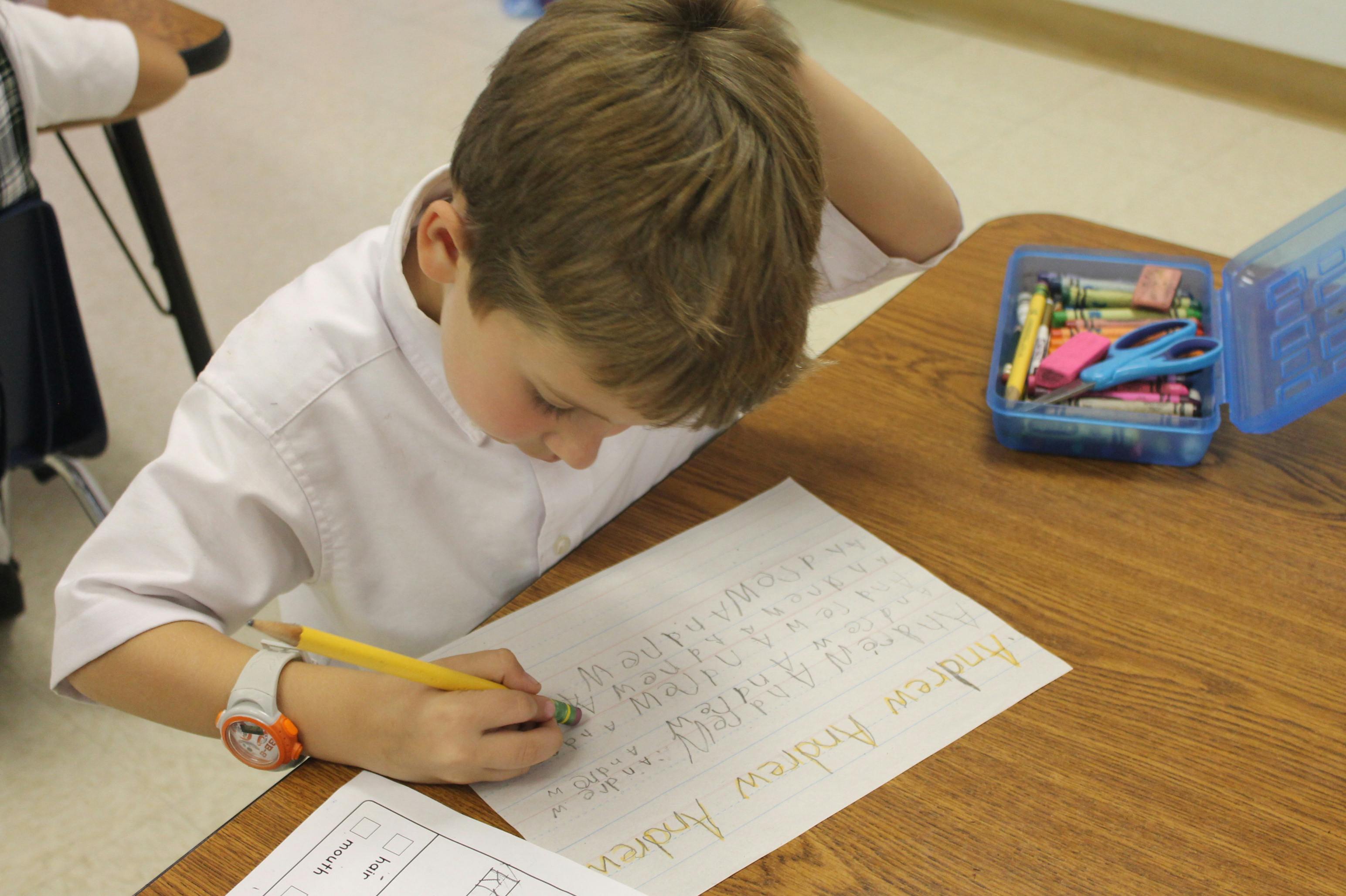 Child writing on paper with a pencil at a desk