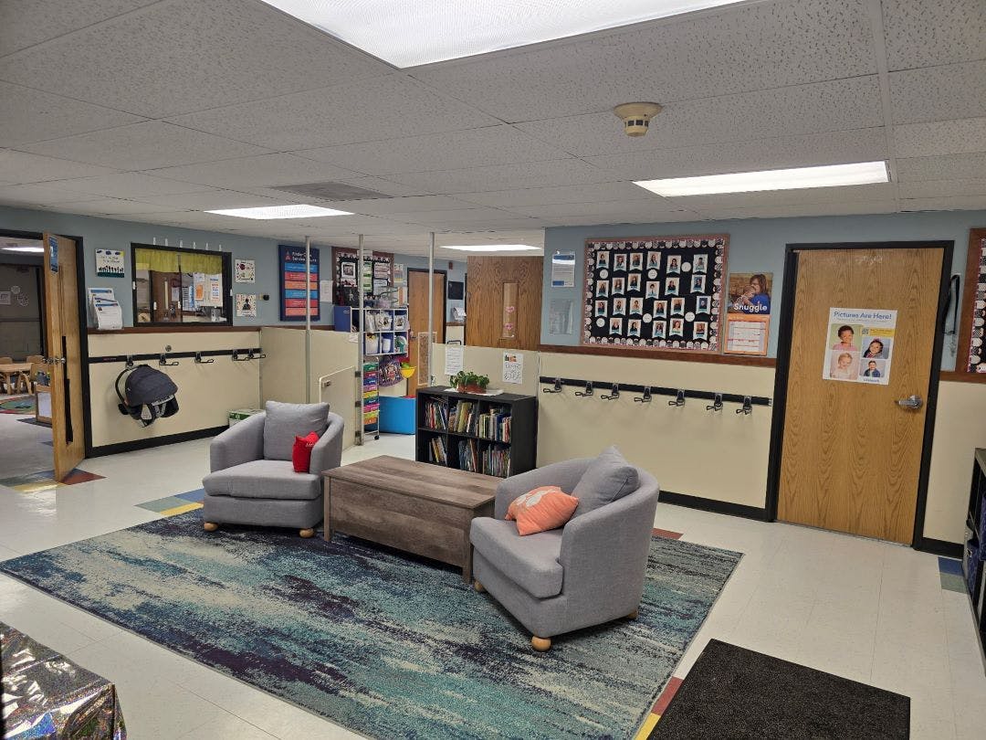 two gray chairs and a wooden coffee table on a colorful rug in a classroom