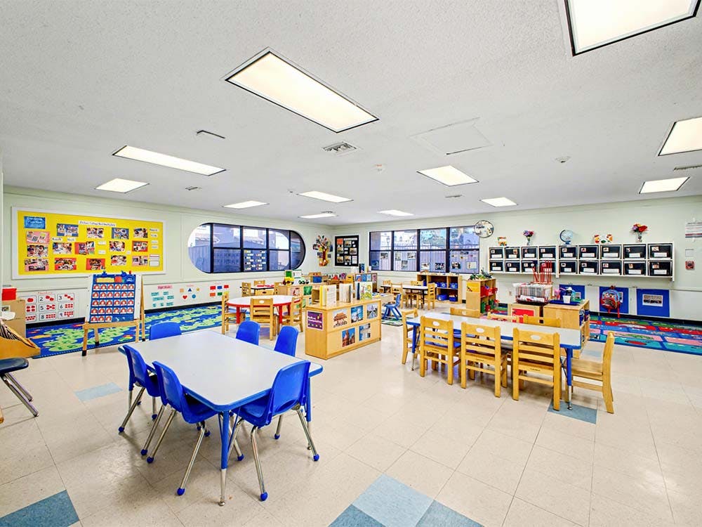 Empty classroom with multiple tables, chairs, and learning materials