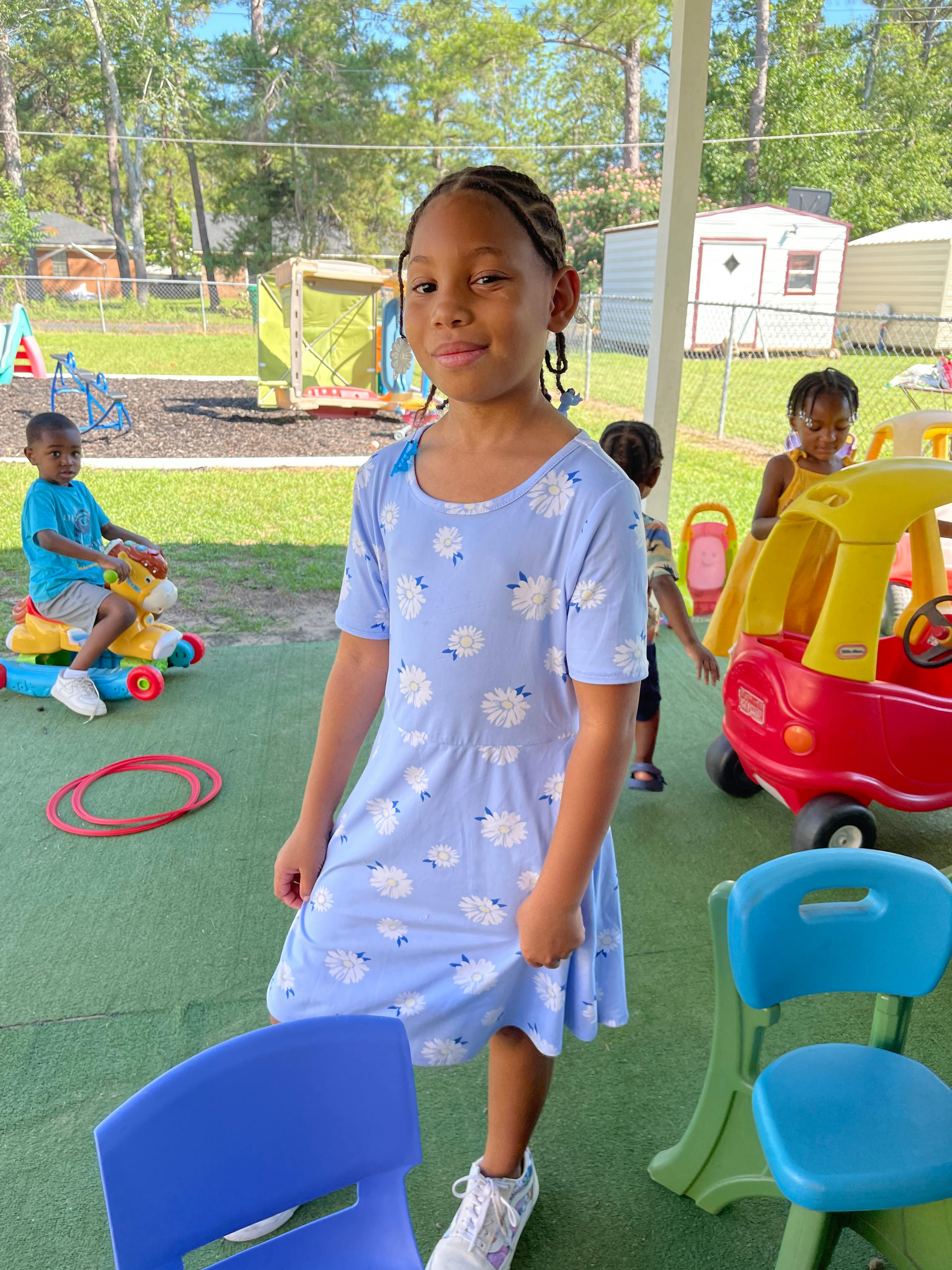 Child standing on a playground with other children playing in the background
