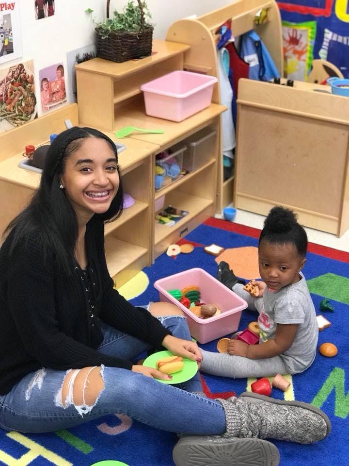 Person and child playing on a rug in a classroom