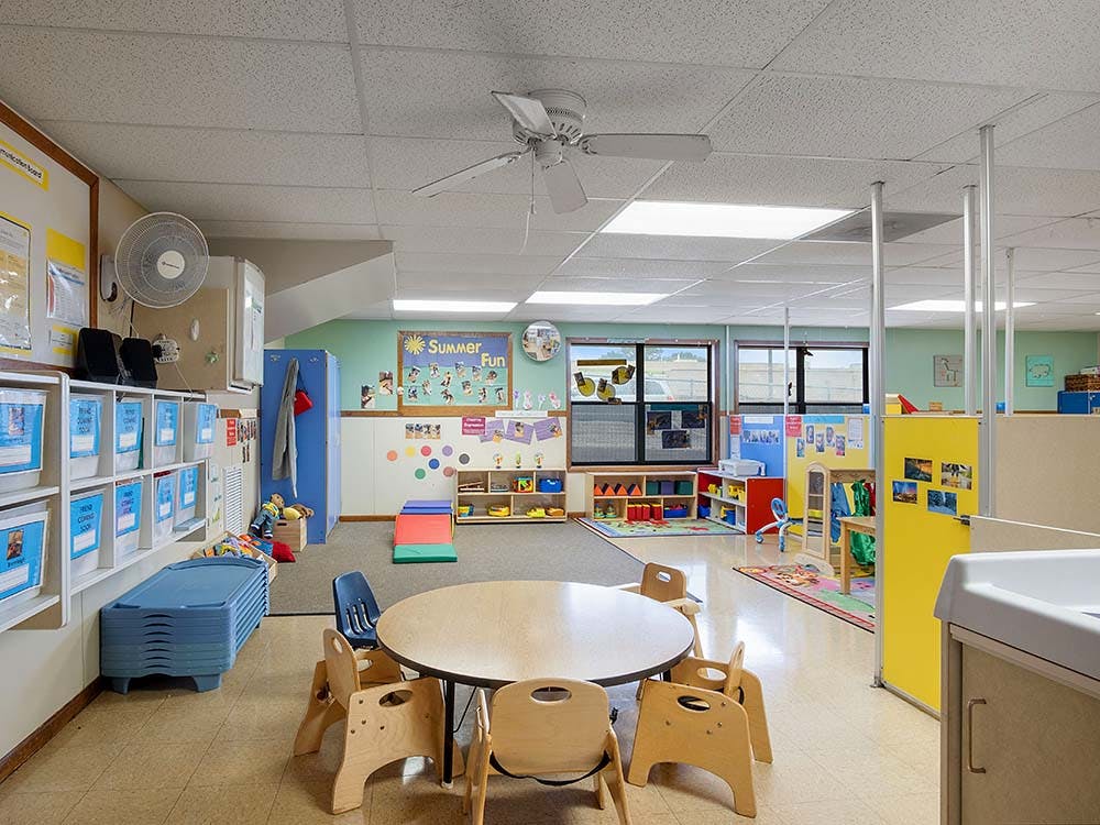 Classroom with small tables and chairs, cubbies, and colorful rugs