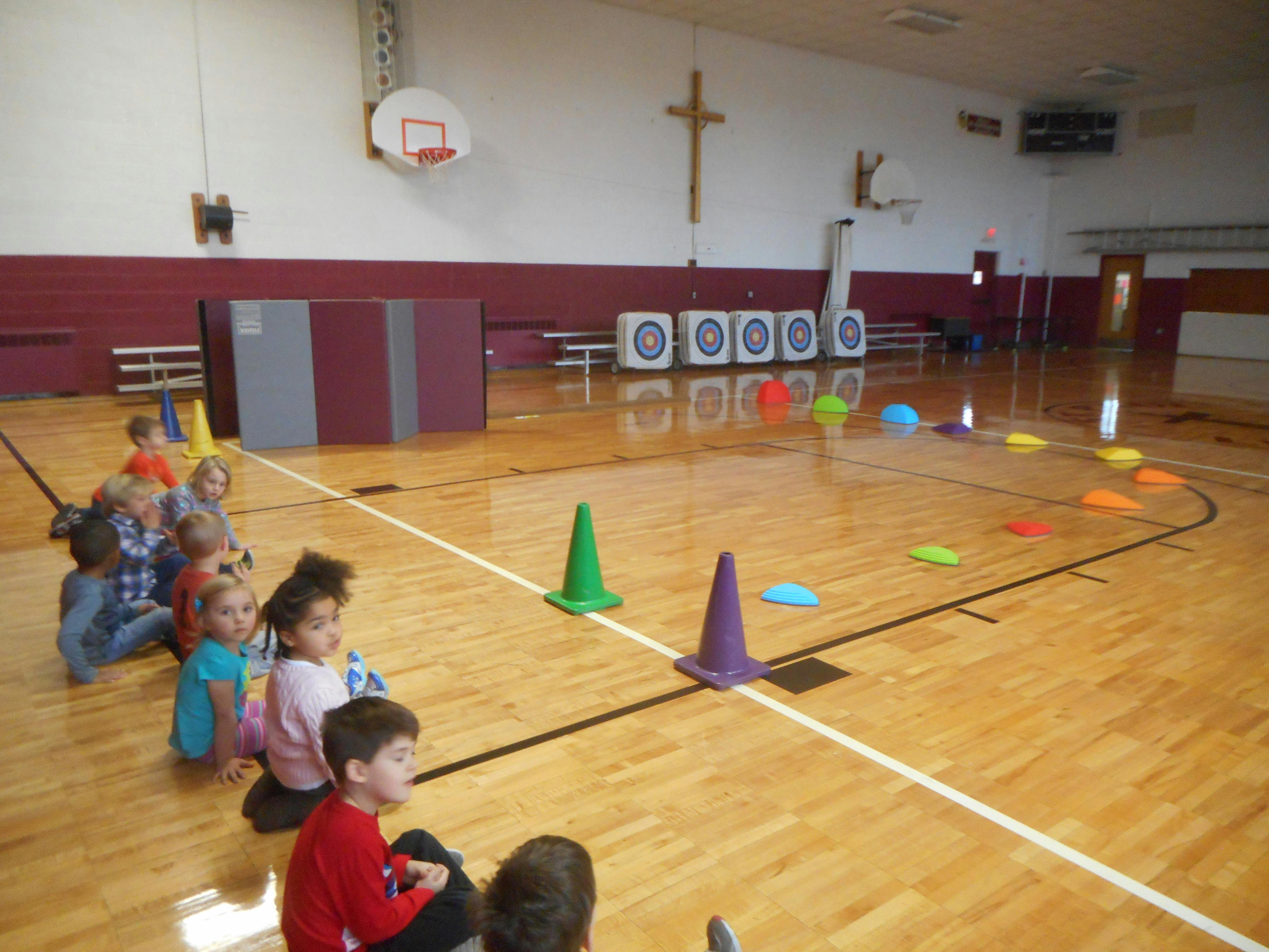 Children sitting on a gymnasium floor with colorful cones and targets