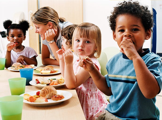 Children eating at a table with an adult nearby