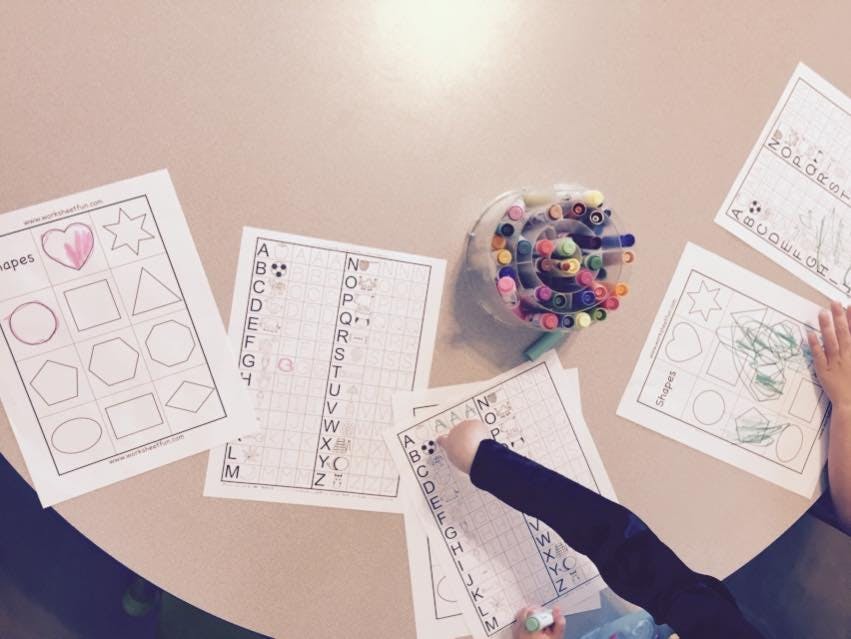 Child's arm coloring on a worksheet with other worksheets and markers on a table