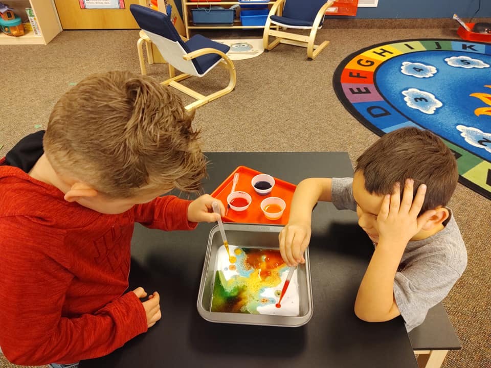 Two children doing a science experiment with colorful liquids in a classroom