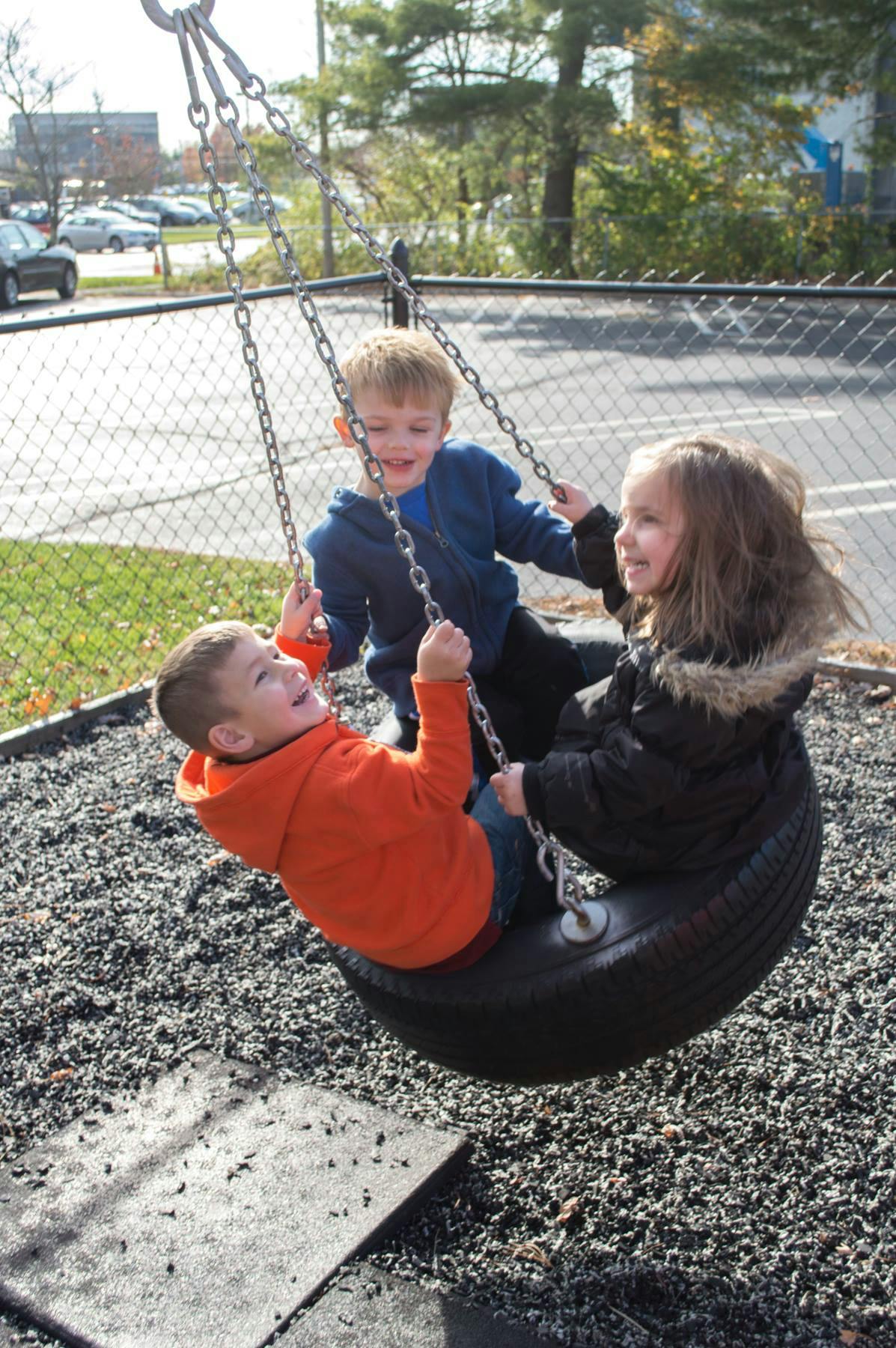 Three children playing on a tire swing