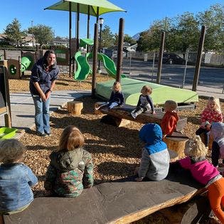 Adult speaking to children seated on logs in a playground