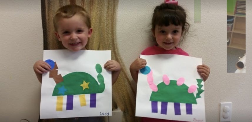Two children holding up paper crafts of dinosaurs