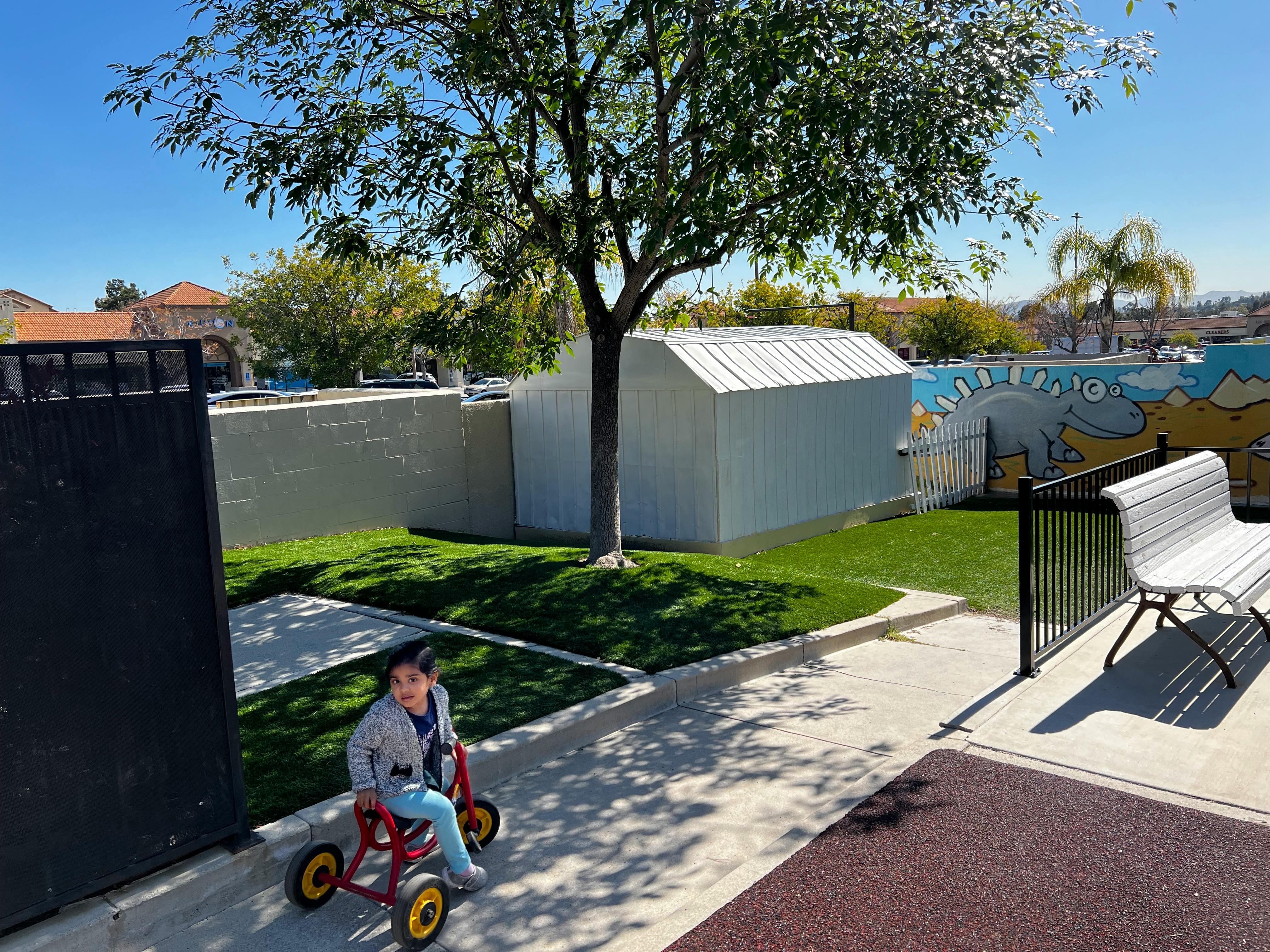 Child riding a tricycle on a paved path next to a grassy area