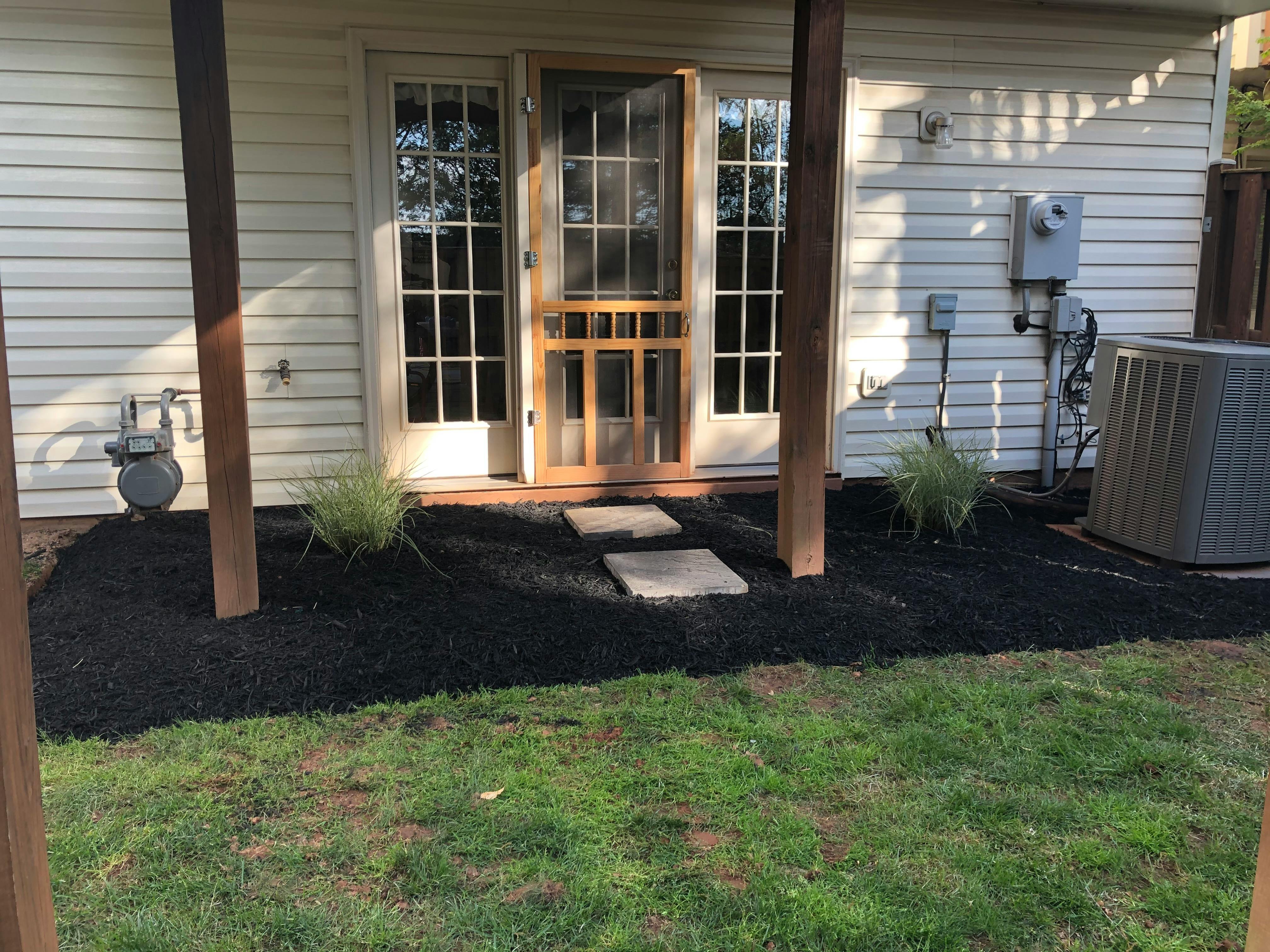 Exterior view of a home entrance with a screen door and mulched garden beds