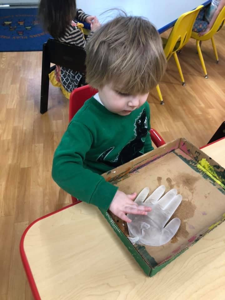 Child in green shirt touching a clear glove in a tray