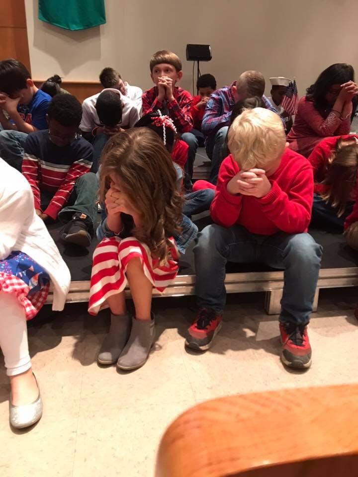 Children sitting with heads bowed and hands clasped