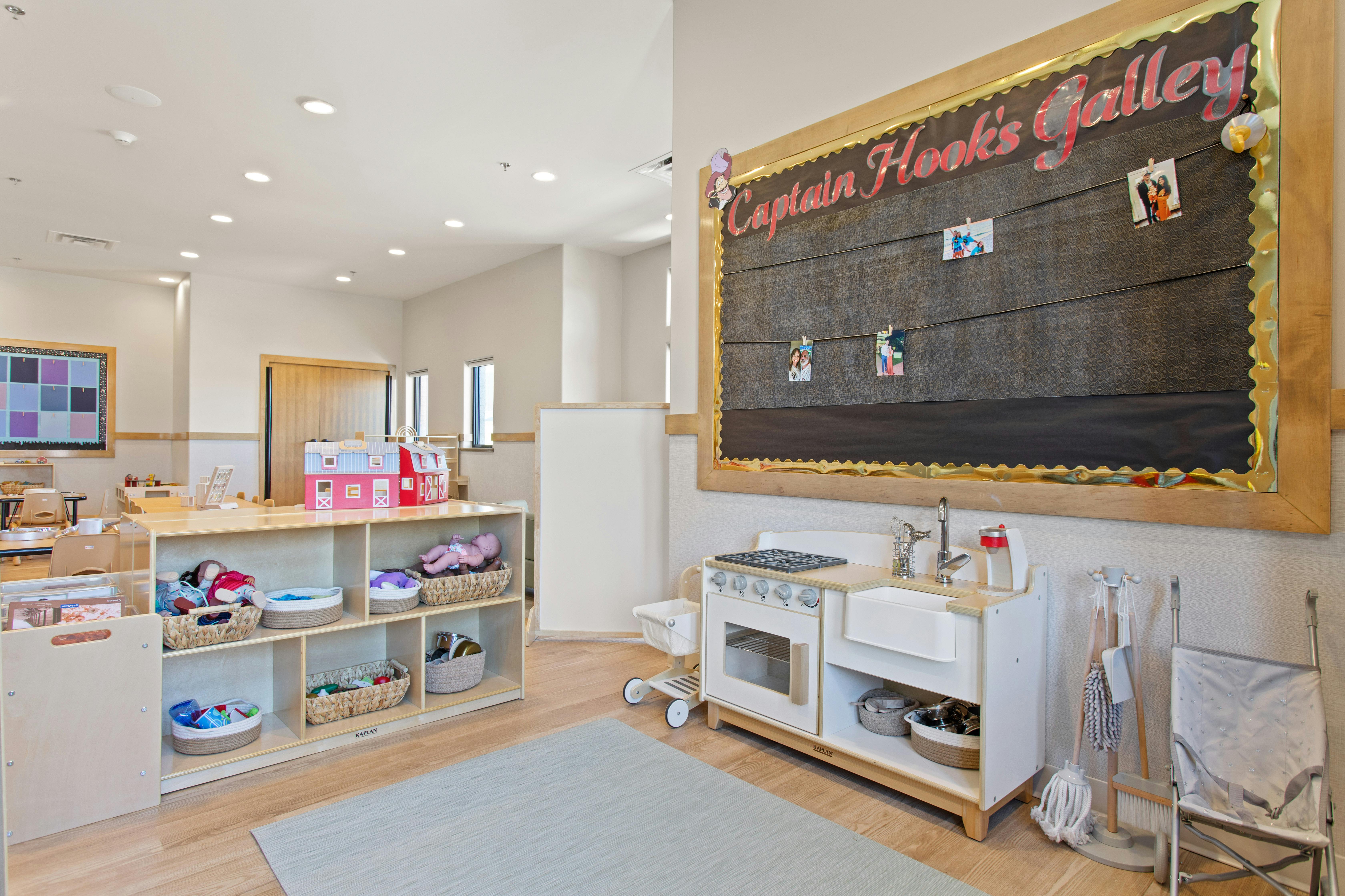 Classroom with shelves of toys and a bulletin board above a play kitchen