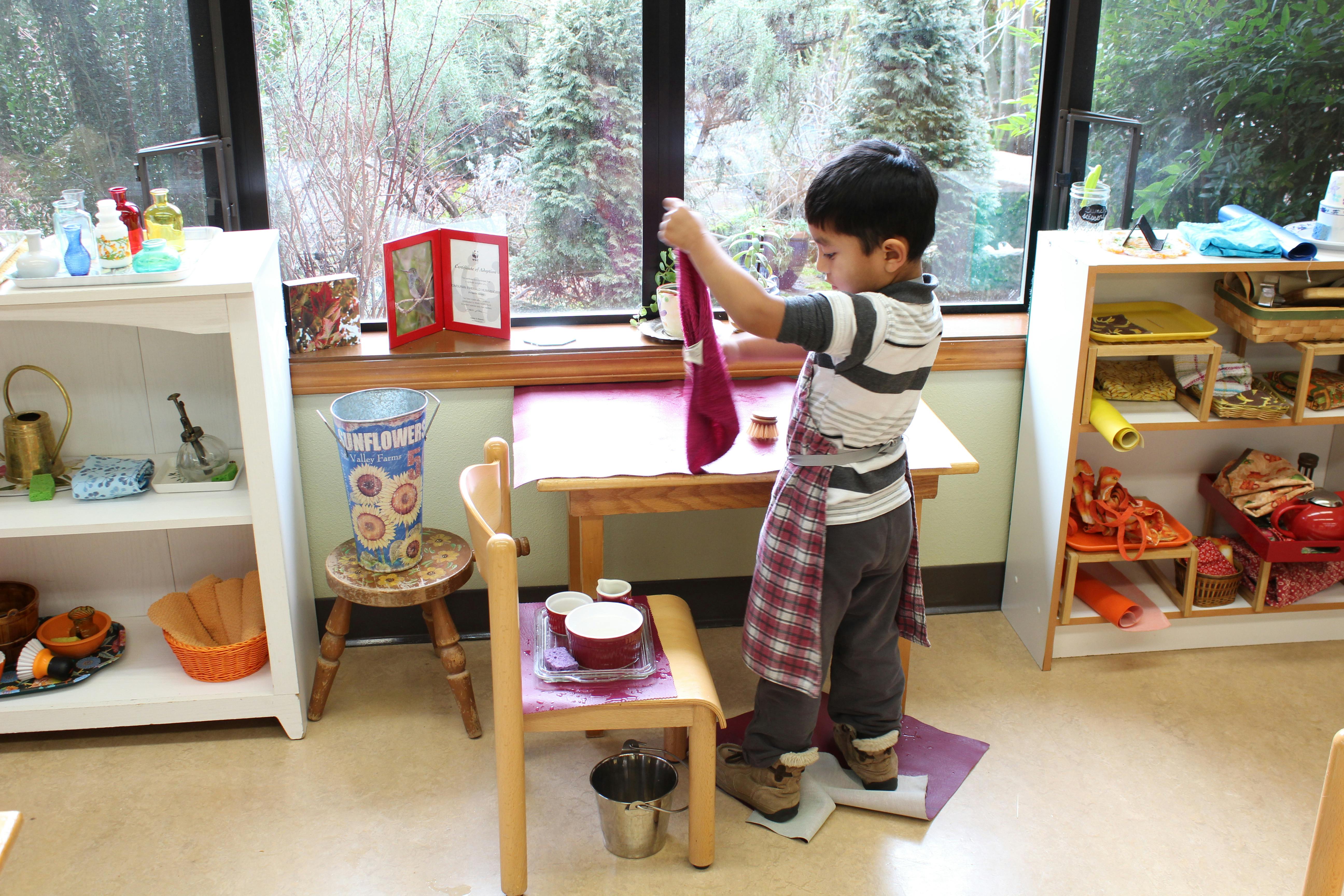 Child wearing an apron drying a dish in a classroom